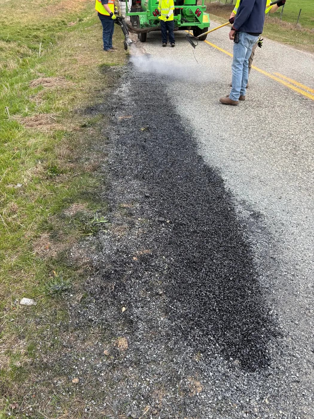 Road crew applying a dark repair treatment along a pavement edge
